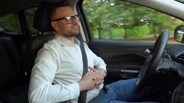 Homem barbudo em óculos e camisa branca dirigindo um carro em tempo ensolarado e usa a função de piloto automático enquanto dirige — Vídeo de Stock