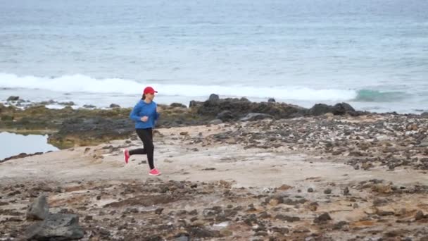 Frau läuft am steinigen Ufer des Ozeans entlang. gesunder aktiver Lebensstil. Zeitlupe — Stockvideo