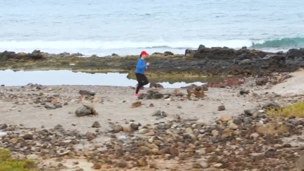 Vrouw loopt langs de stenige kust van de oceaan. Gezonde actieve levensstijl — Stockvideo
