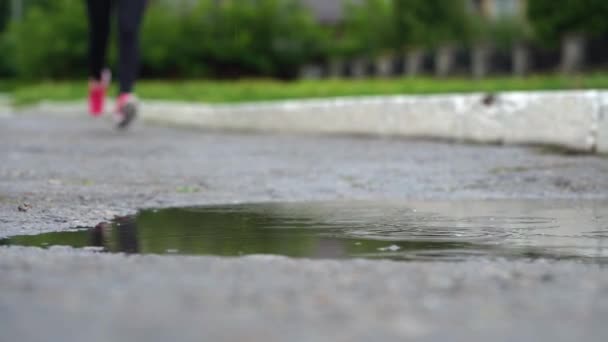 Πόδια ενός δρομέα σε αθλητικά παπούτσια. Αθλητική γυναίκα τρέξιμο σε εξωτερικούς χώρους, πατώντας σε λασπωμένη λακκούβα. Ένας δρομέας που τρέχει στη βροχή, κάνοντας βουτιά — Αρχείο Βίντεο