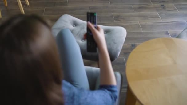 Nő ül egy széken, tévézni, zöld képernyő, kapcsolási csatornák távirányítóval. Chroma kulcs. Beltéri — Stock videók