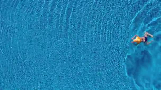 Vue du haut comme une femme en maillot de bain bleu et un grand chapeau jaune nage dans la piscine — Video