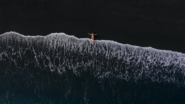 Draufsicht einer Frau im roten Badeanzug, die an einem schwarzen Strand an der Brandungslinie liegt. Küste der Insel Teneriffa, Kanarische Inseln, Spanien. — Stockvideo