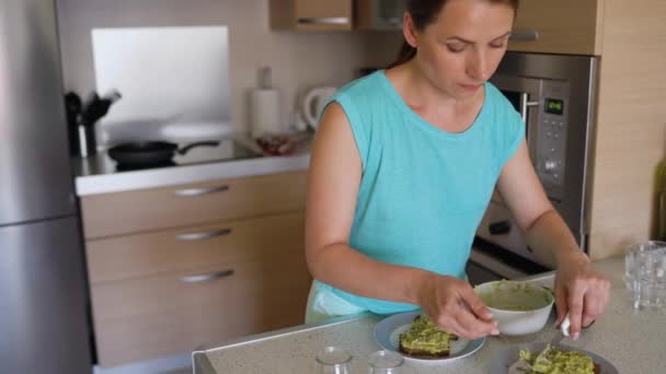 Женщина готовит тост с авокадо - накладывает нарезанный авокадо на хлеб из цельного зерна — стоковое видео