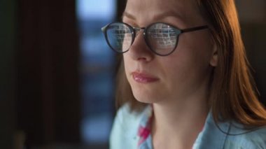 Gözlüklü kadın monitöre bakıyor ve internette sörf yapıyor. Monitör ekranı gözlüklere yansıyor. Gece çalış. İçişleri Bakanlığı. Uzak çalışma