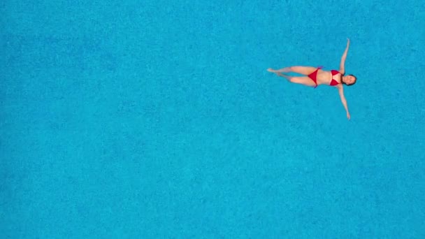 Вид сверху на женщину в красном купальнике, лежащую на спине в бассейне. Расслабляющая концепция — стоковое видео