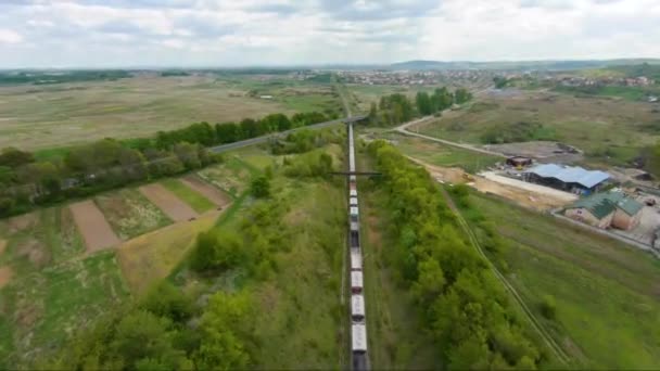 El dron FPV vuela rápido y maniobrable por encima de un tren de mercancías en movimiento. Camino del automóvil en el fondo — Vídeo de stock