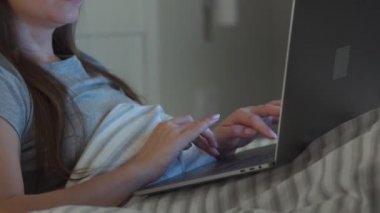 Gözlüklü kadın geceleri yatakta yatarken dizüstü bilgisayarda çalışıyor. İnternet bağımlısı veya uykusuzluk konsepti.