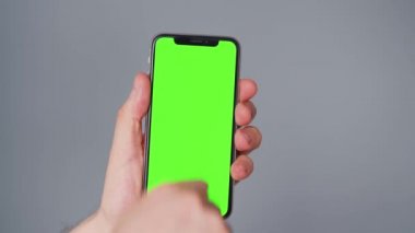 Gri arka planda yeşil ekranlı akıllı telefon kullanan erkek eller. Krom anahtar