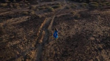 Mavi elbiseli bir kadının havadan görünüşü çölün ortasında tek başına dönüyor. Meditasyon ve nefes alma pratiği. Doğayla birlik. Tenerife, Kanarya Adaları, İspanya