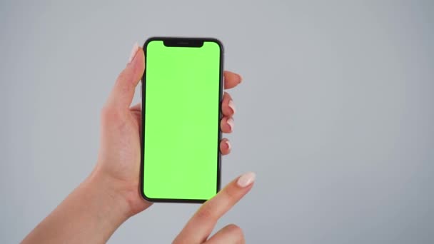 여성들은 스마트폰을 사용 합니다. 회색 배경에 녹색 화면이 있는 스마트폰이죠. 크로마 키. — 비디오