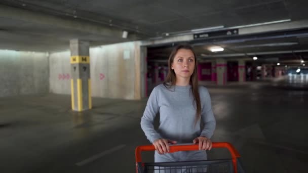 Mujer pasa por un estacionamiento subterráneo con un carrito de compras — Vídeos de Stock