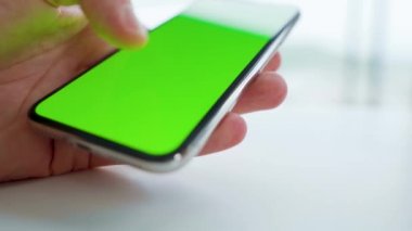 Beyaz masadaki yeşil ekranlı akıllı telefonu kullanan erkek eller. Krom anahtar