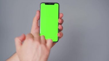 Gri arka planda yeşil ekranlı akıllı telefon kullanan erkek eller. Krom anahtar