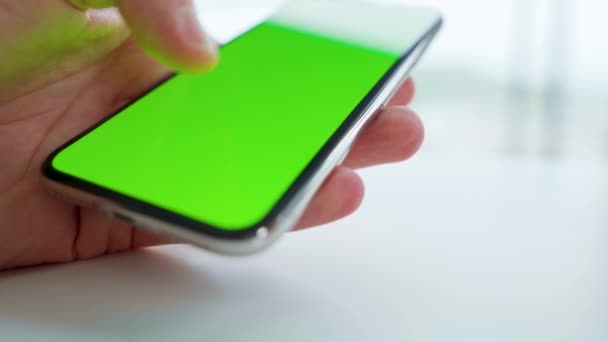 Manos masculinas usando un teléfono inteligente con una pantalla verde en una mesa blanca. Clave de croma — Vídeos de Stock