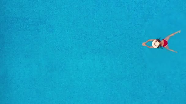 Blick von oben, als eine Frau in rotem Badeanzug und Hut im Pool schwimmt — Stockvideo