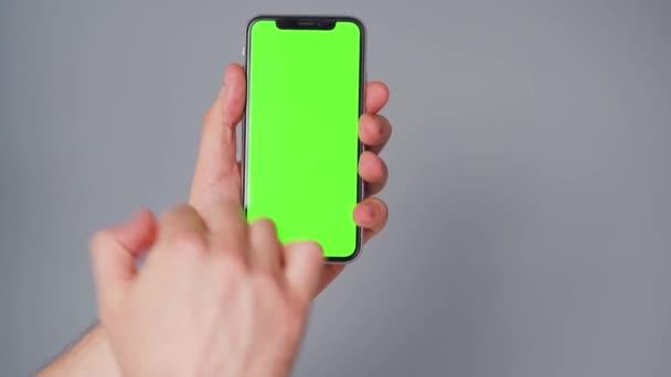 회색 배경에 녹색 화면이 달린 스마트폰을 사용하는 남성의 손. 크로마 키 — 비디오