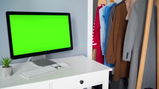 Estúdio criativo - monitor de computador com uma tela verde em primeiro plano. A mulher escolhe roupas ao fundo. Chave Chroma. Espaço de cópia. — Vídeo de Stock