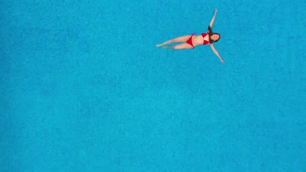 Вид зверху як жінка в червоному купальнику, що лежить на спині в басейні. Розслаблююча концепція — стокове відео