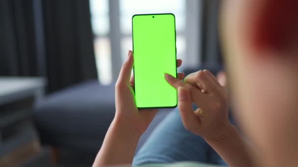 Žena doma leží na pohovce a používá smartphone se zelenou maketou obrazovky ve vertikálním režimu. Dívka procházející internet, sledující obsah, videa, blogy. POV. — Stock video