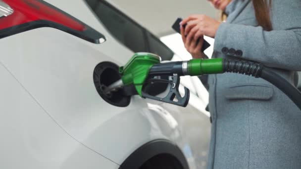 Mujer usando smartphone mientras su coche está repostando. Movimiento lento — Vídeos de Stock