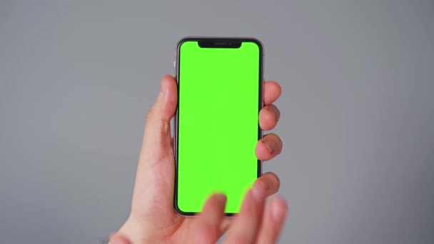 회색 배경에 녹색 화면이 달린 스마트폰을 사용하는 남성의 손. 크로마 키 — 비디오