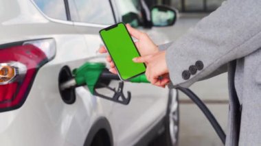 Kadın, bir arabaya yakıt ikmali için akıllı telefondan mobil uygulama kullanıyor. Yeşil ekranlı akıllı telefon. Krom anahtar