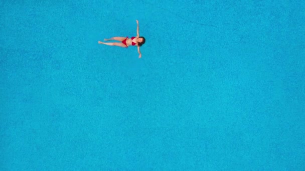 Вид зверху як жінка в червоному купальнику, що лежить на спині в басейні. Розслаблююча концепція — стокове відео