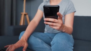 Kadın rahat bir kanepede oturuyor ve bir dizüstü bilgisayar ve akıllı telefon üzerinde çalışıyor. Uzak çalışma kavramı.