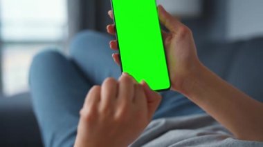Evde bir kadın kanepeye uzanıyor ve dikey modda yeşil ekran ile akıllı telefon kullanıyor. İnternette gezinen, içerik izleyen, videolar, bloglar. POV.