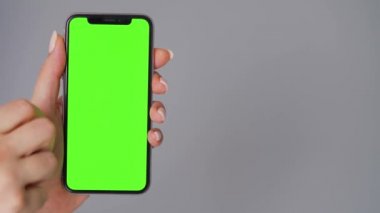 Gri arka planda yeşil ekranlı akıllı telefon kullanan kadın eller. Krom anahtar.