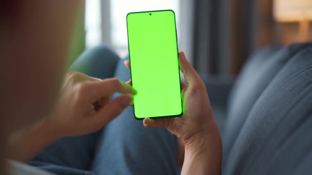 Vrouw thuis liggend op een bank en met behulp van smartphone met groene mock-up scherm in verticale modus. Meisje surfen op internet, kijken naar inhoud, video 's, blogs. POV. — Stockvideo