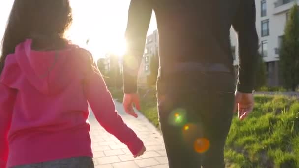 Táta a dcera se procházejí po okolí při západu slunce. Dítě drží otce za ruku. — Stock video