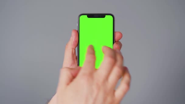 Férfi kezek egy okostelefonnal, zöld képernyővel, szürke háttérrel. Kroma kulcs — Stock videók