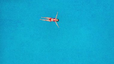 Yukarıdan bakıldığında kırmızı mayo giymiş bir kadın havuzda sırtüstü yatıyor. Rahatlatıcı kavram