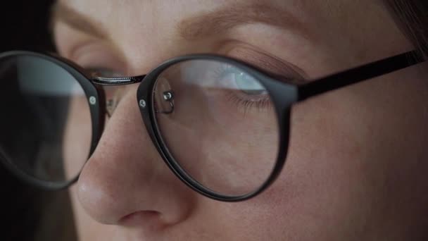Woman in glasses looking on the monitor and surfing Internet. The monitor screen is reflected in the glasses. Work at night. Home Office. Remote work — Stock Video