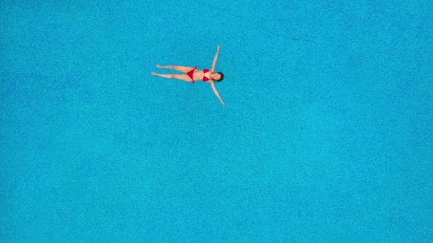Θέα από την κορυφή ως γυναίκα με κόκκινο μαγιό ξαπλωμένη στην πλάτη της στην πισίνα. Χαλαρωτική έννοια — Αρχείο Βίντεο