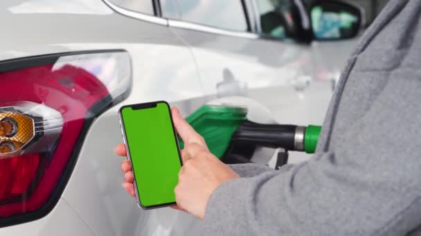 Mujer utiliza una aplicación móvil en un teléfono inteligente para pagar por repostar un coche. Smartphone con pantalla verde. Clave de croma — Vídeos de Stock