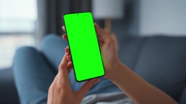 Evde bir kadın kanepeye uzanıyor ve dikey modda yeşil ekran ile akıllı telefon kullanıyor. İnternette gezinen, içerik izleyen, videolar, bloglar. POV.