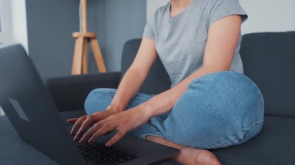 Egy nő ül egy kényelmes kanapén, és egy laptopon dolgozik. A távmunka fogalma. — Stock videók