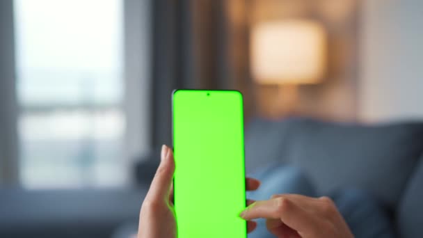 Kvinna hemma ligger på en soffa och använder smartphone med grön mock-up skärm i vertikalt läge. Flicka surfa på Internet, titta på innehåll, videor, bloggar. Födelsedatum. — Stockvideo