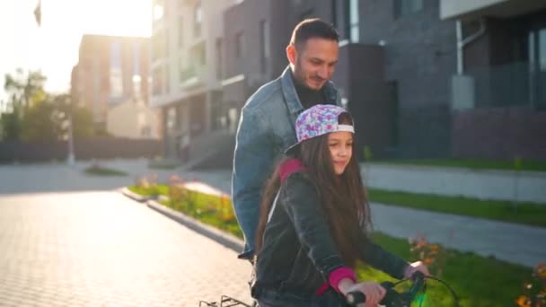 Tata uczy córkę jeździć na rowerze o zachodzie słońca. Szczęśliwy ojciec cieszy się, że jego córka nauczyła się jeździć na rowerze. Zwolniony ruch — Wideo stockowe
