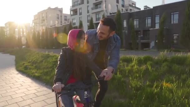 Papa bringt der Tochter bei, wie man bei Sonnenuntergang Fahrrad fährt. Glücklicher Vater freut sich, dass seine Tochter Radfahren gelernt hat. — Stockvideo