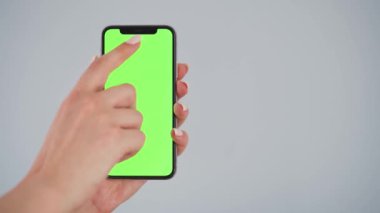 Gri arka planda yeşil ekranlı akıllı telefon kullanan kadın eller. Krom anahtar.
