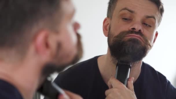 사람은 전기 조련사를 사용하여 수염을 깎는다. 거울에 비친 반사 — 비디오