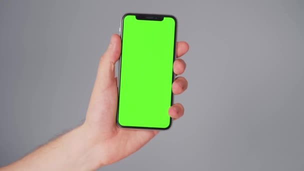 Αρσενικά χέρια χρησιμοποιώντας ένα smartphone με πράσινη οθόνη σε γκρι φόντο. Κλειδί χρωμίου — Αρχείο Βίντεο