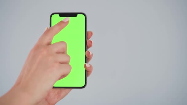 Weibliche Hände mit einem Smartphone mit grünem Bildschirm auf grauem Hintergrund. Chroma-Schlüssel. — Stockvideo