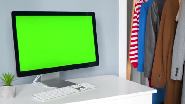 Estúdio criativo - monitor de computador com uma tela verde em primeiro plano. A mulher escolhe roupas ao fundo. Chave Chroma. Espaço de cópia. — Vídeo de Stock