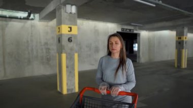 Kadın elinde alışveriş arabasıyla yeraltı otoparkından geçiyor.