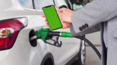 Kadın, bir arabaya yakıt ikmali için akıllı telefondan mobil uygulama kullanıyor. Yeşil ekranlı akıllı telefon. Krom anahtar